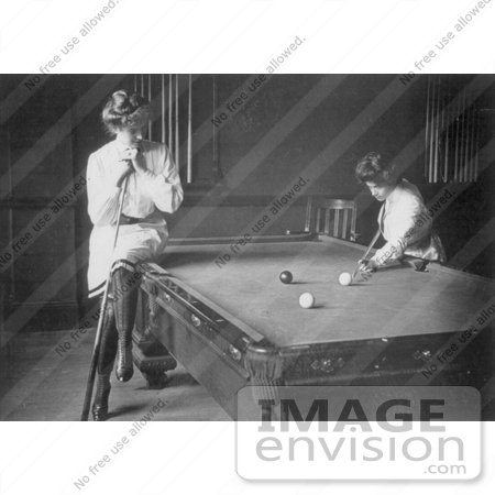 #21643 Stock Photography of a Woman Resting on the Edge of a Pool Table, Leaning on a Cue Stick While Watching Her Friend Play by JVPD
