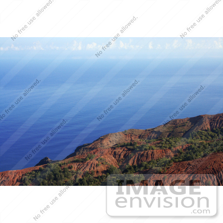 #36525 Stock Photo of Red Na Pali Coast Cliffs Looking Over Rippling Blue Waters Of The Pacific Oceanm With Clouds In The Distance by Jamie Voetsch