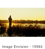 #15563 Picture Of A Duck Hunter Standing In Reeds Against An Orange Sunrise