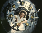 Photo of a Riveter Woman Framed by a Circular Opening of a Cowling, Working on Lower Section